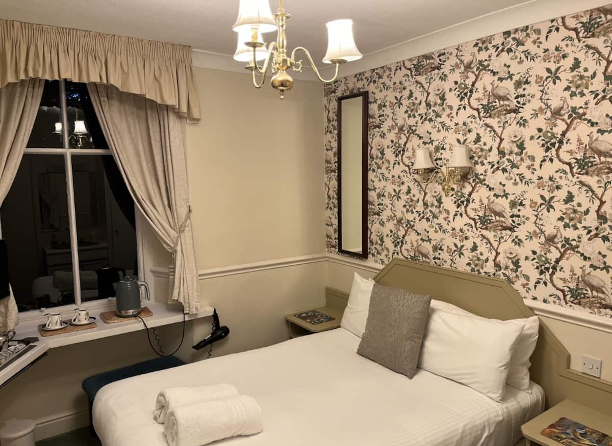 A comfortable double room with elegant botanical wallpaper, crisp white linen and a tea & coffee tray