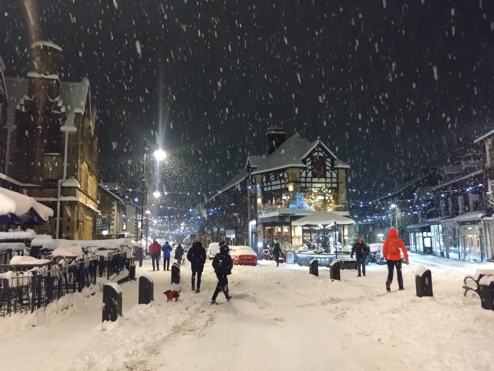 Windermere village under heavy snowfall at night, with Christmas lights glowing along the street